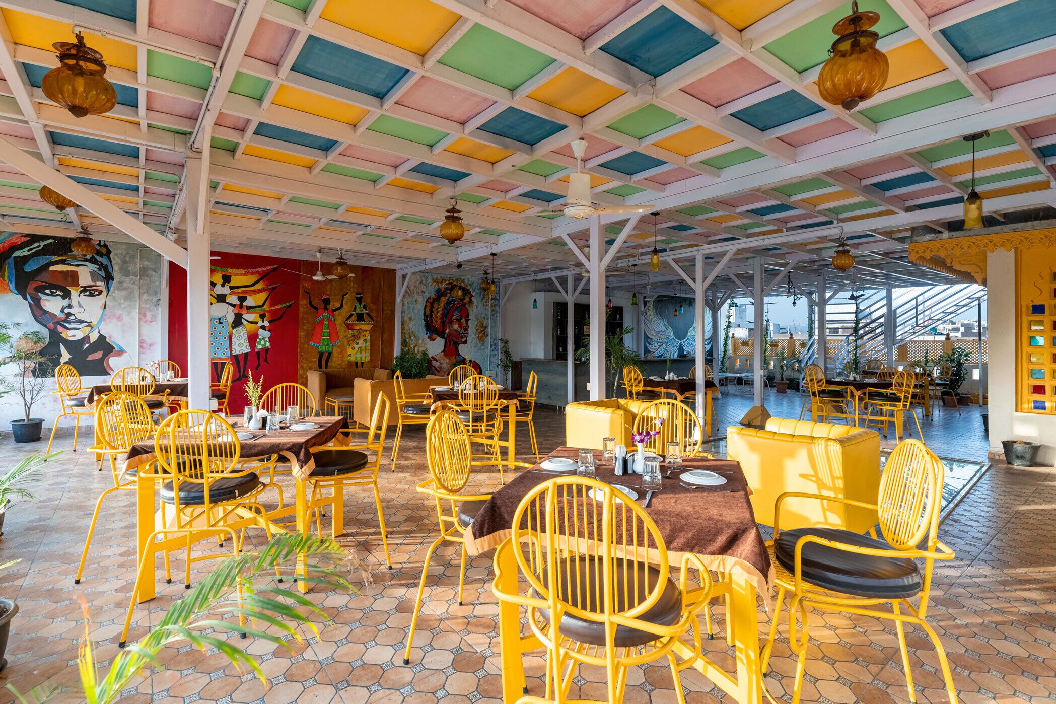 Un espace de restauration intérieur avec des chaises et des tables jaunes, un plafond coloré et des peintures murales.