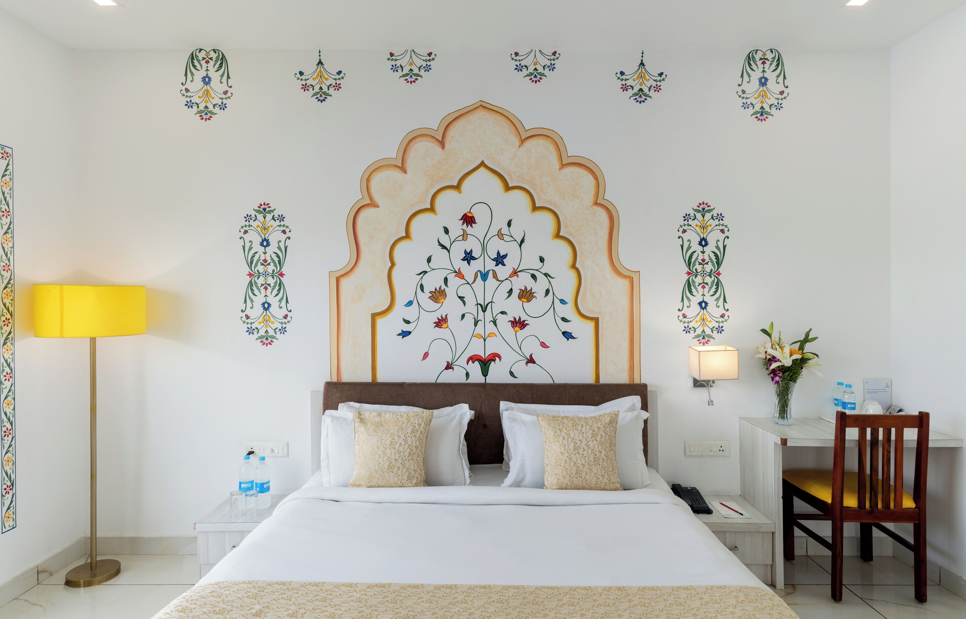 A hotel room with a large bed, a desk, a chair, a lamp, and decorative wall art.
