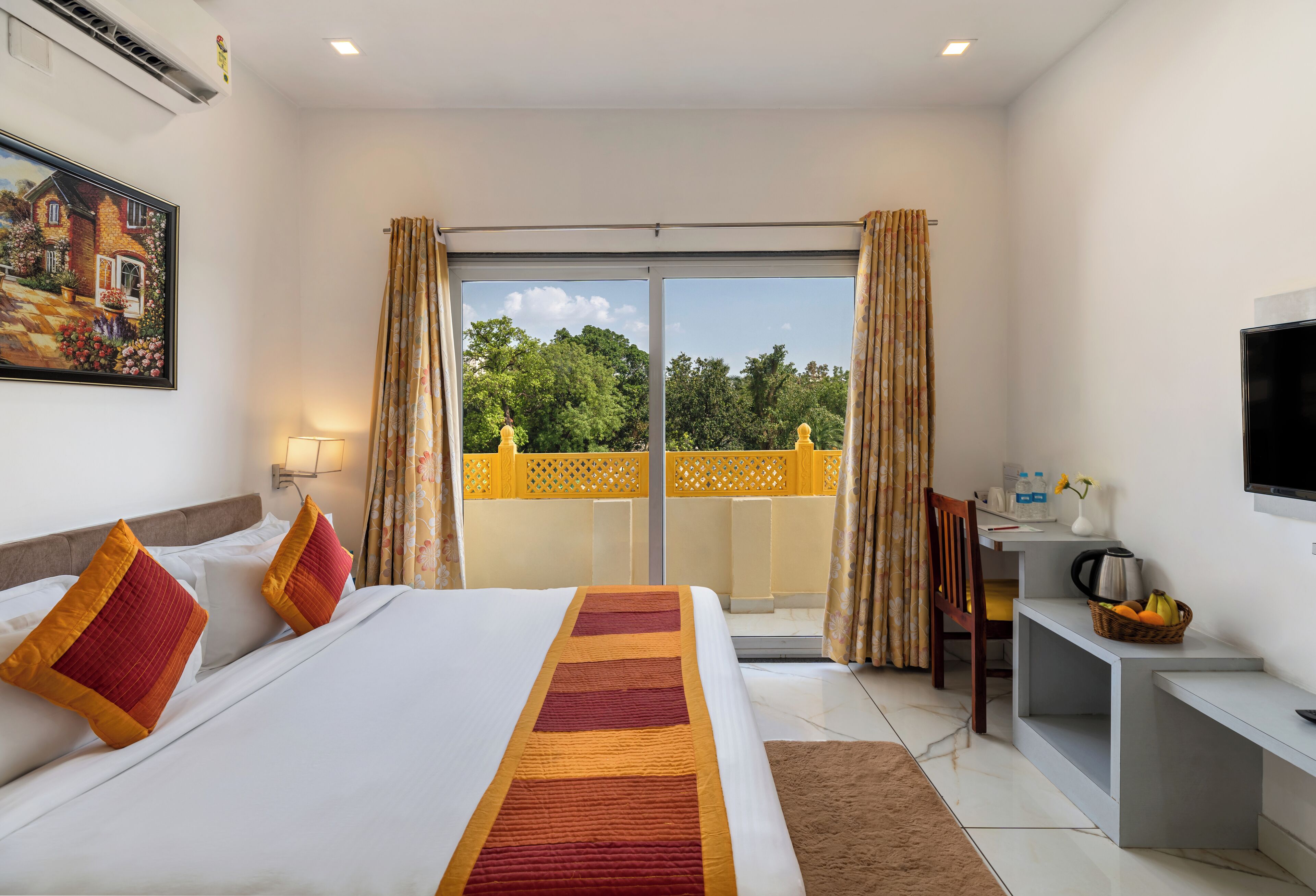 A hotel room with a large bed, a desk, a TV, and a balcony with curtains.