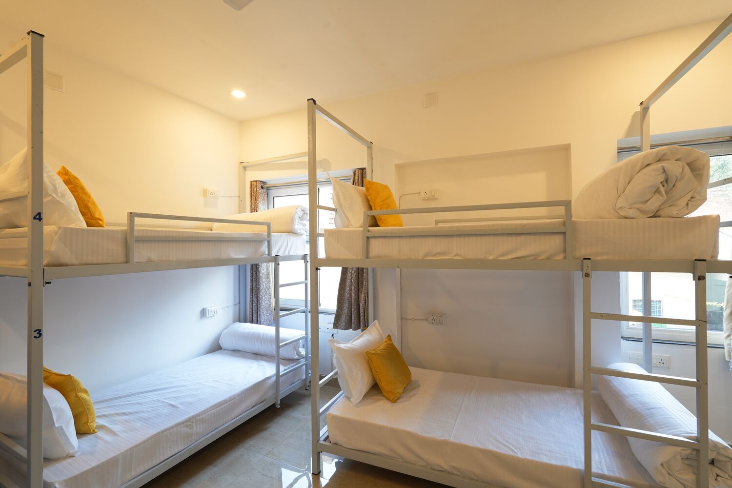 A dormitory room with bunk beds, each with a pillow and a blanket.
