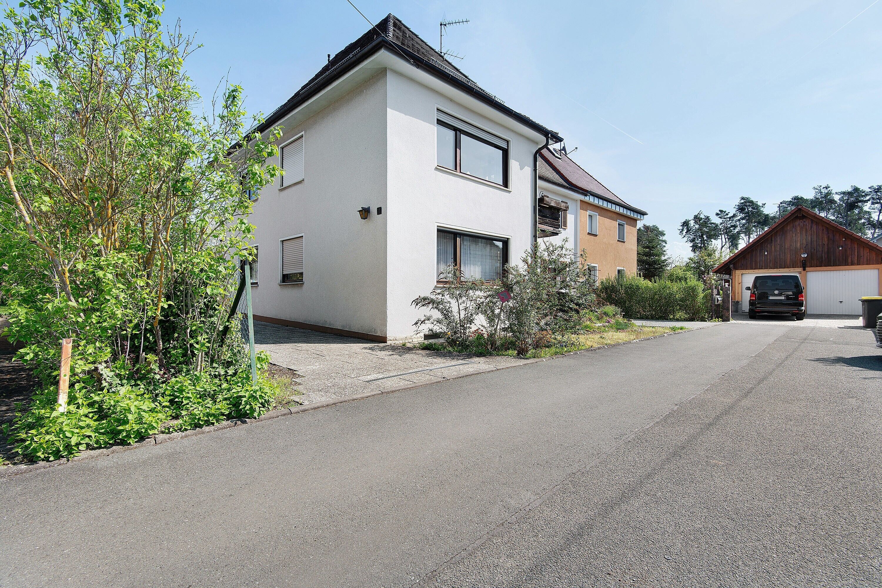 A two-story house with a garage, a driveway, and a garden with various plants.