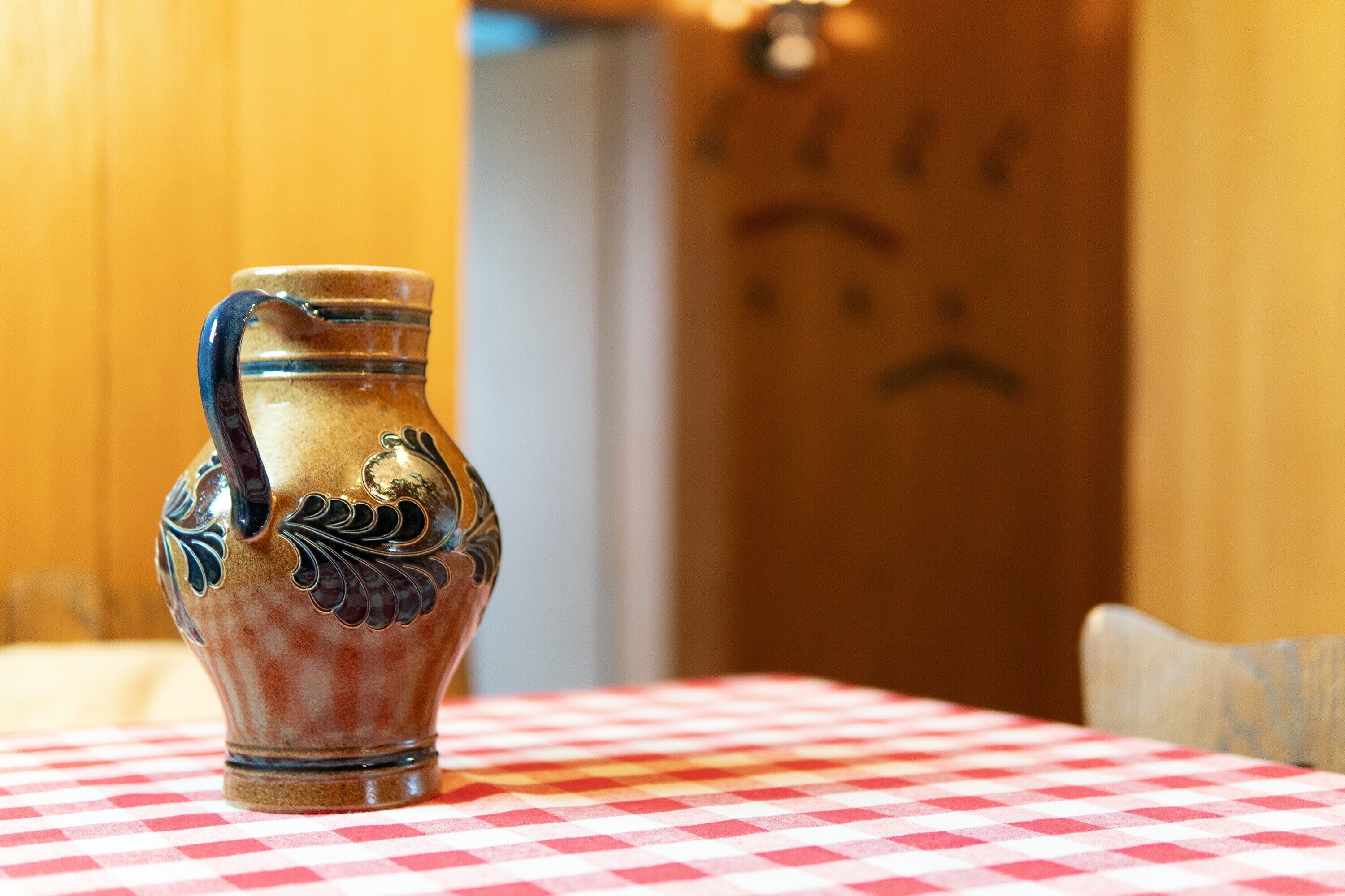A ceramic vase with floral designs on a table with a checkered tablecloth.