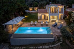 A two-story house with a swimming pool, outdoor seating, and a stone wall.