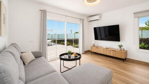 Ein modernes Wohnzimmer mit einem grauen Sofa, einem kleinen schwarzen Couchtisch, einer Holz-TV-Konsole und einem großen Fernseher.