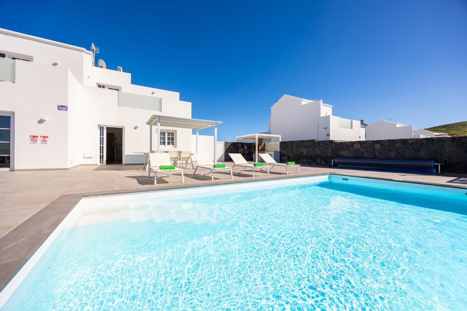 Un espace piscine moderne avec une eau d’un bleu limpide, des bâtiments blancs et des chaises longues.