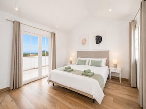 A bedroom with a bed, two bedside tables, a window with curtains, and artwork on the wall.