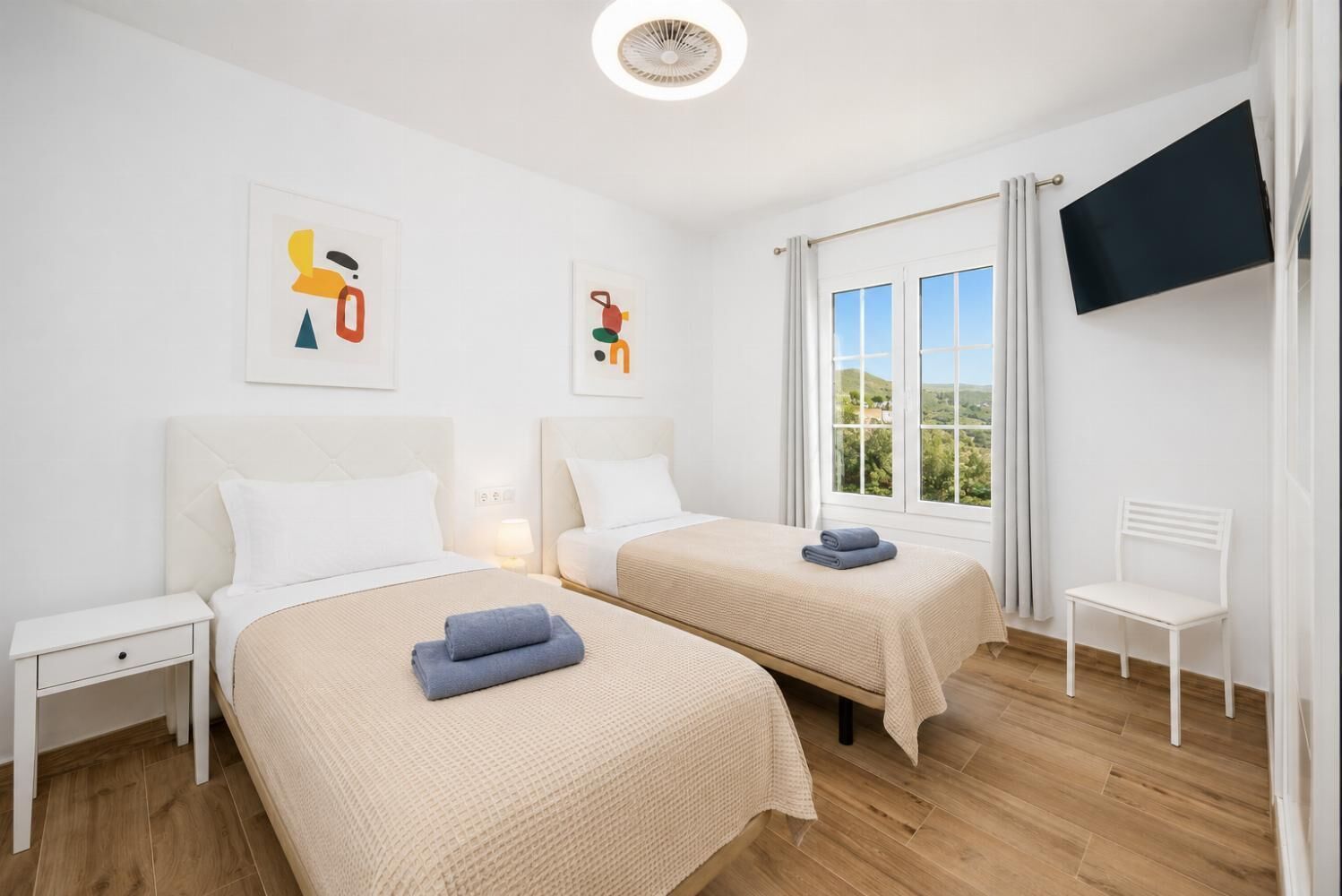A hotel room with two beds, a TV, and a window with a view.