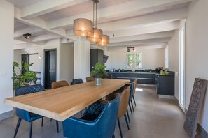 Un grand espace à manger avec une table en bois et des chaises bleues, une cuisine dotée de meubles sombres et d’un éclairage suspendu.