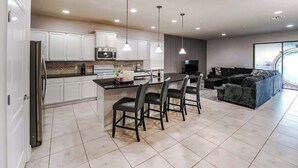 A modern kitchen with white cabinets, a central island with chairs, and a dining area.