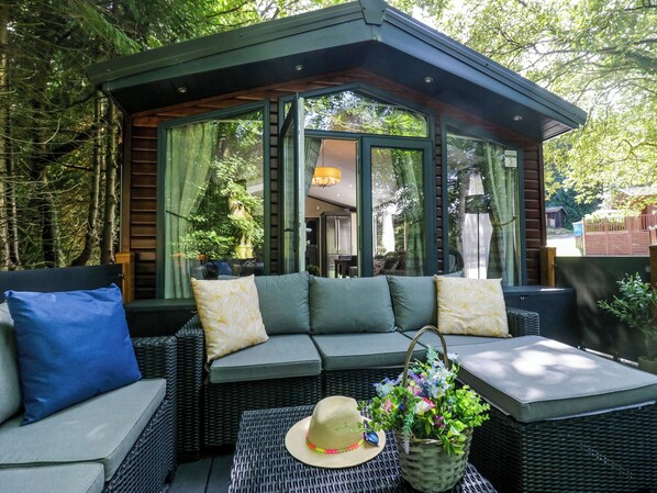 A covered outdoor seating area with a sofa and cushions, a wicker table, and a basket of flowers.