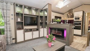 Una sala de estar moderna con televisor de pantalla plana, estanterías empotradas, chimenea y una zona de cocina con horno.