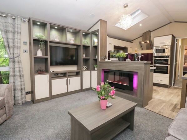 Una sala de estar moderna con televisor de pantalla plana, estanterías empotradas, chimenea y una zona de cocina con horno.