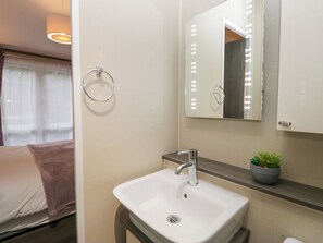 Un baño moderno con un lavamanos blanco, un espejo con iluminación, un sujetarrepisas para toallas y una pequeña planta en maceta.
