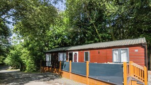 A small, single-story wooden cabin with a fenced deck, surrounded by dense trees. - Feather Hill Lodge White Cross Bay, Skiptory Howe 38 (Windermere)