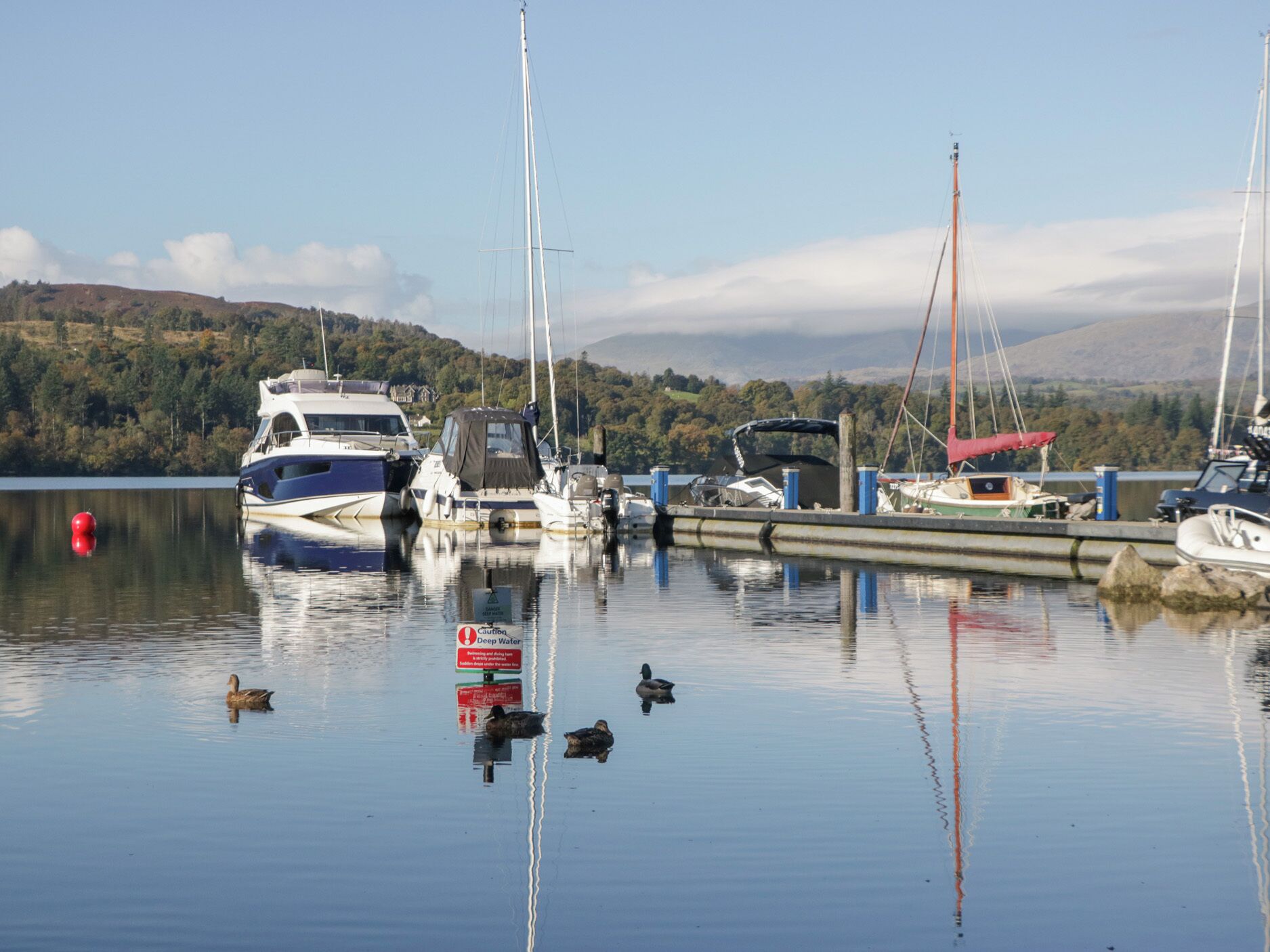 Un port de plaisance avec des bateaux amarrés, une eau calme et un panneau d’avertissement indiquant la présence d’une zone à grande profondeur.