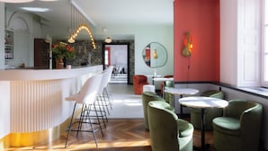 Uma área de bar moderna com balcão curvo, banquetas brancas e cadeiras estofadas em verde.