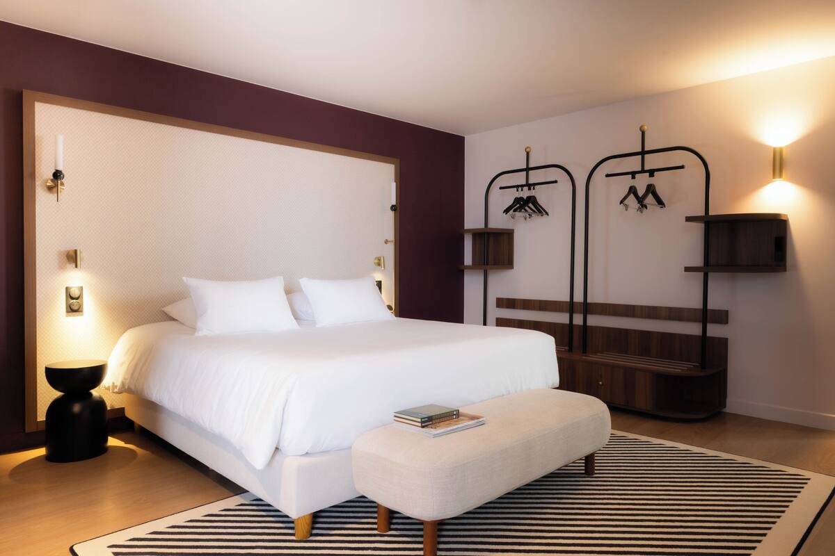 A modern bedroom with a large bed, bedside tables, a reading bench, and wall-mounted lighting.