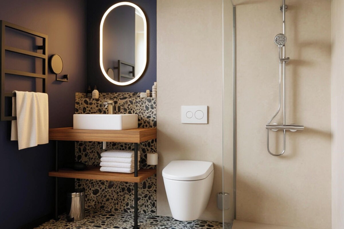 Un baño moderno con un lavamanos independiente, inodoro, ducha y espejo con marco iluminado.