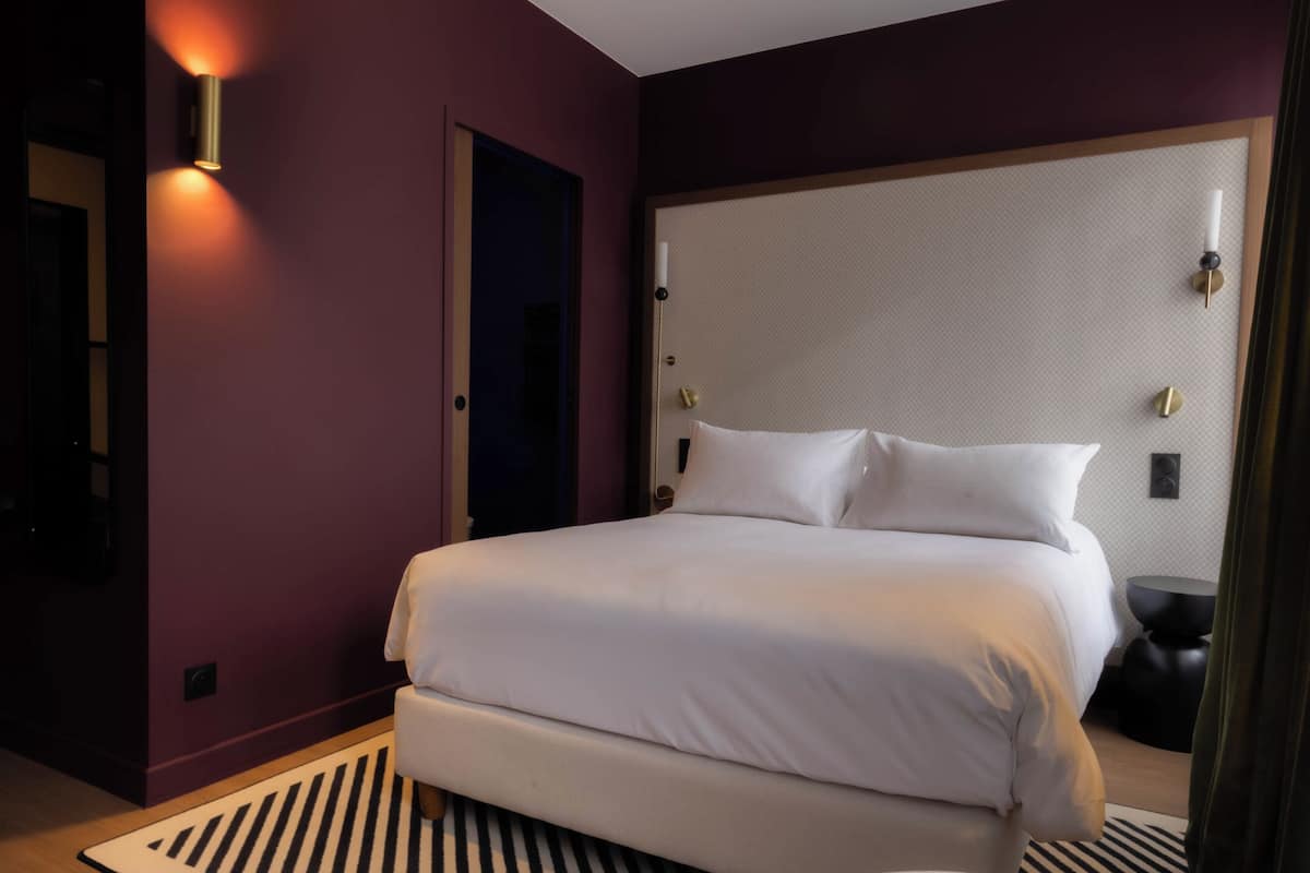 A hotel room with a large bed, a headboard with wall-mounted lights, a bedside table, and a striped rug.