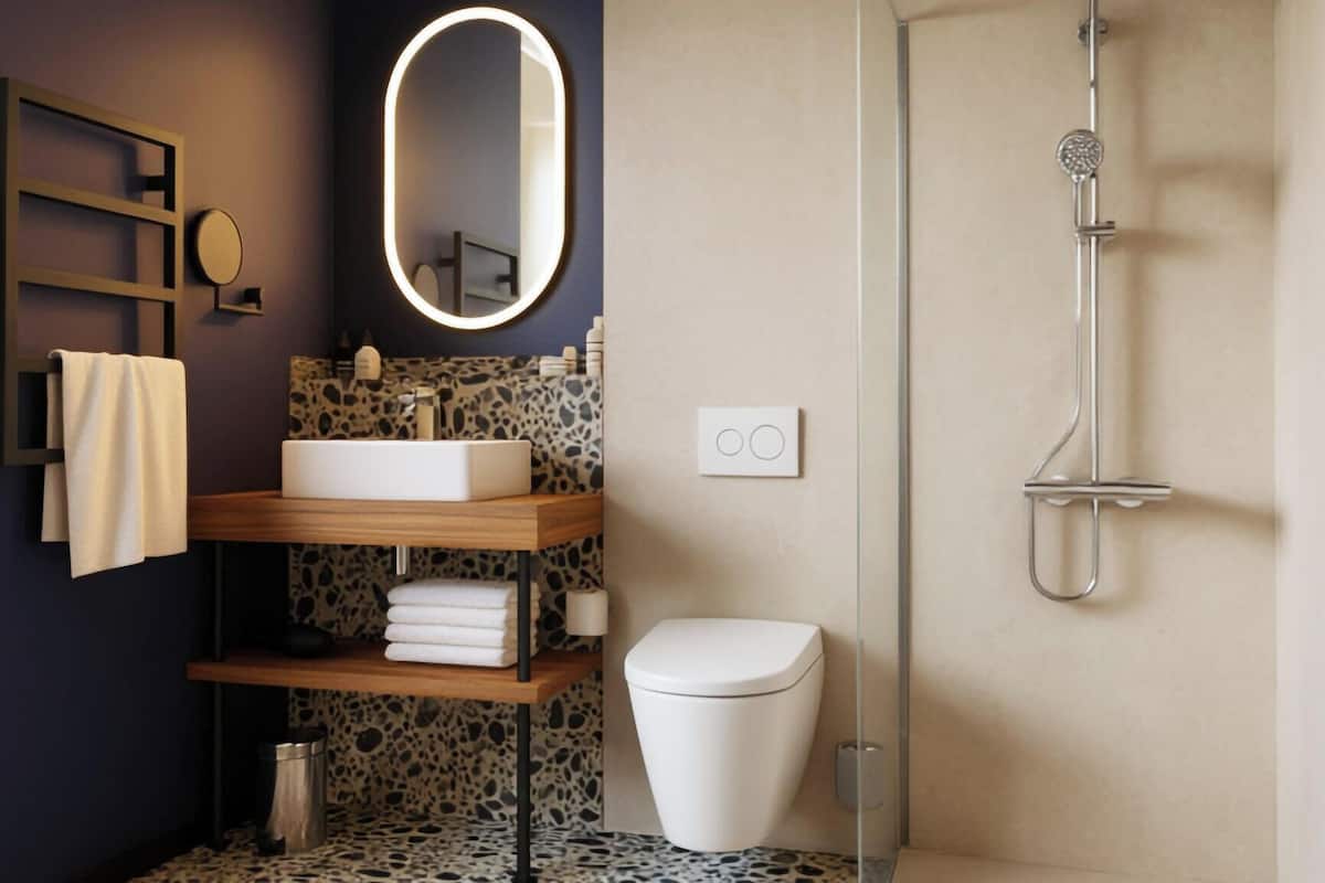 Ein modernes Badezimmer mit einem freistehenden Waschbecken, einer Toilette, einer Dusche und einem Spiegel mit beleuchtetem Rahmen.