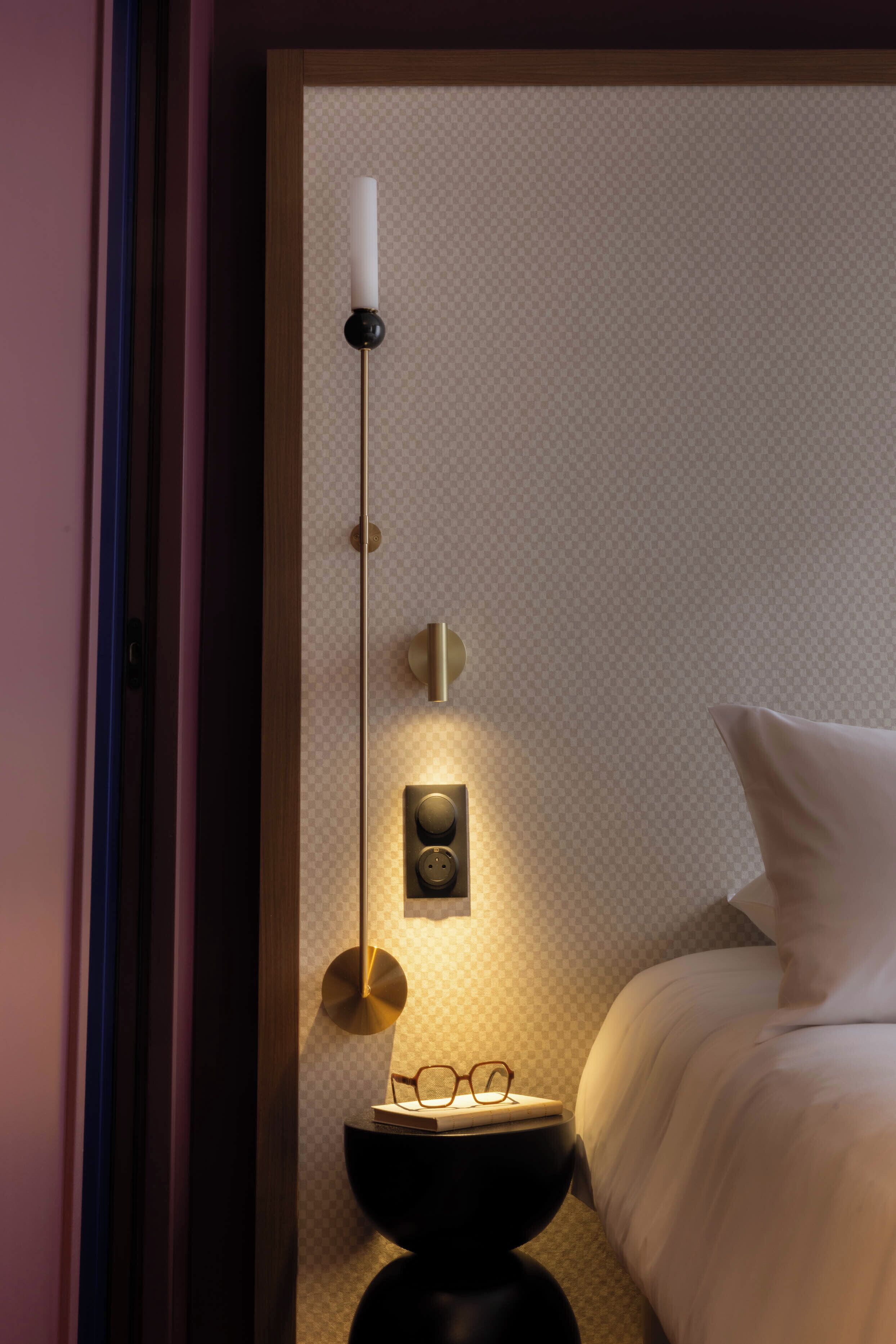 Un dormitorio con cama, mesita de noche y lámpara de pared.