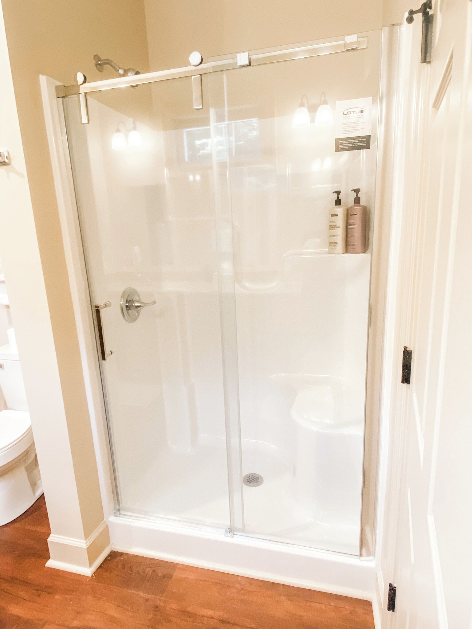 A glass-enclosed shower with a white door, a visible drain, and a white toilet visible through the glass.