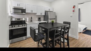 Uma cozinha compacta com armários brancos, bancada preta e um espaço de refeições com mesa e cadeiras pretas.