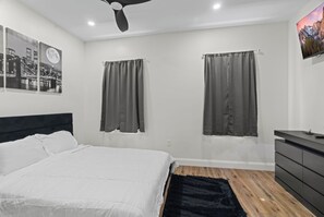 A modern bedroom with a large bed, two windows with curtains, a ceiling fan, a mounted TV, and a dresser. - Modern 2 Bedroom 1 Bath Unit 2 Near Airport, Xfinity Arena And Eagles Stadium (Philadelphia)