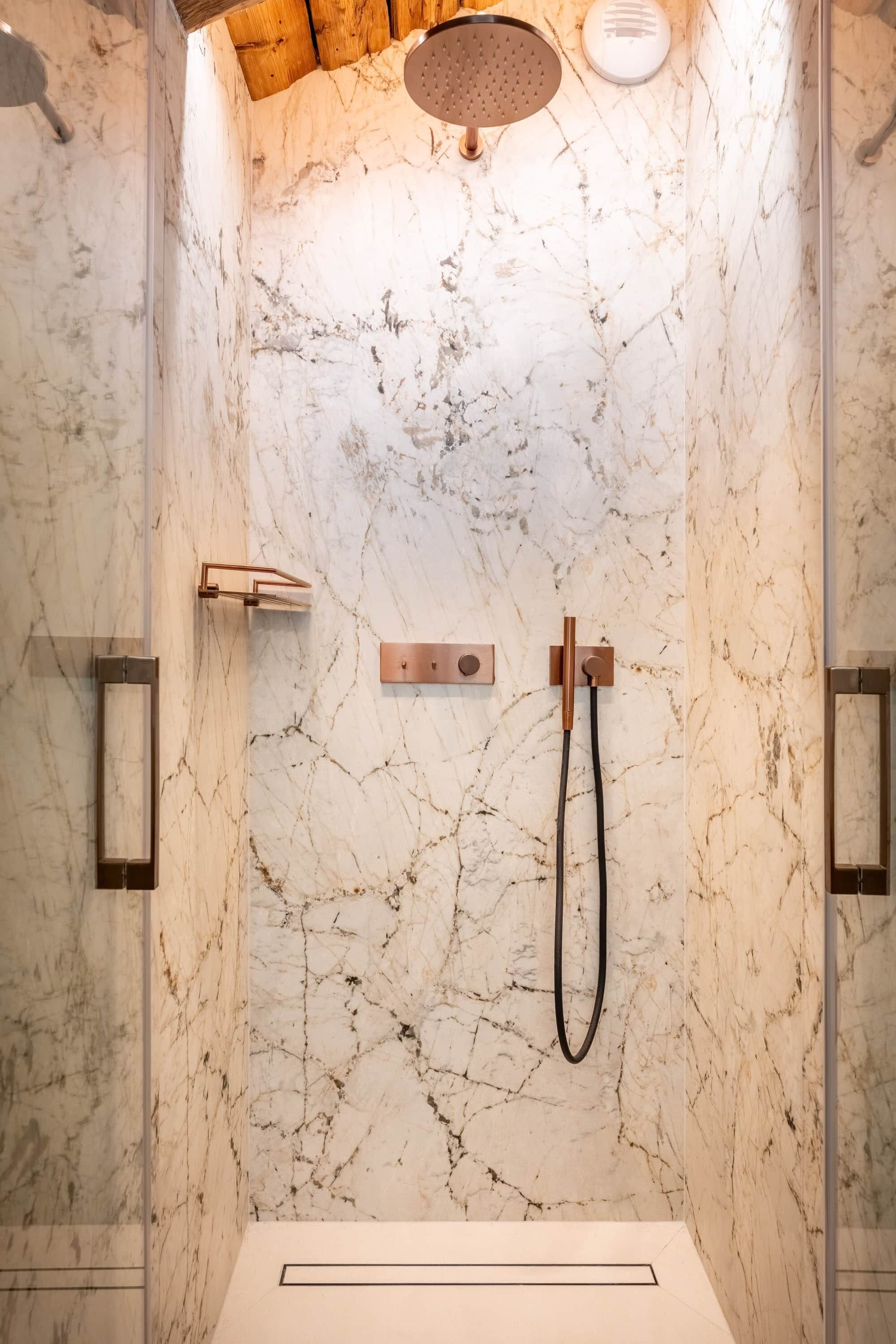 A modern shower with a marble wall, a handheld showerhead, and a wall-mounted control panel.