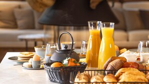 A breakfast table with pastries, juice, and a coffee pot, set against a rustic stone wall and a sofa in the background.