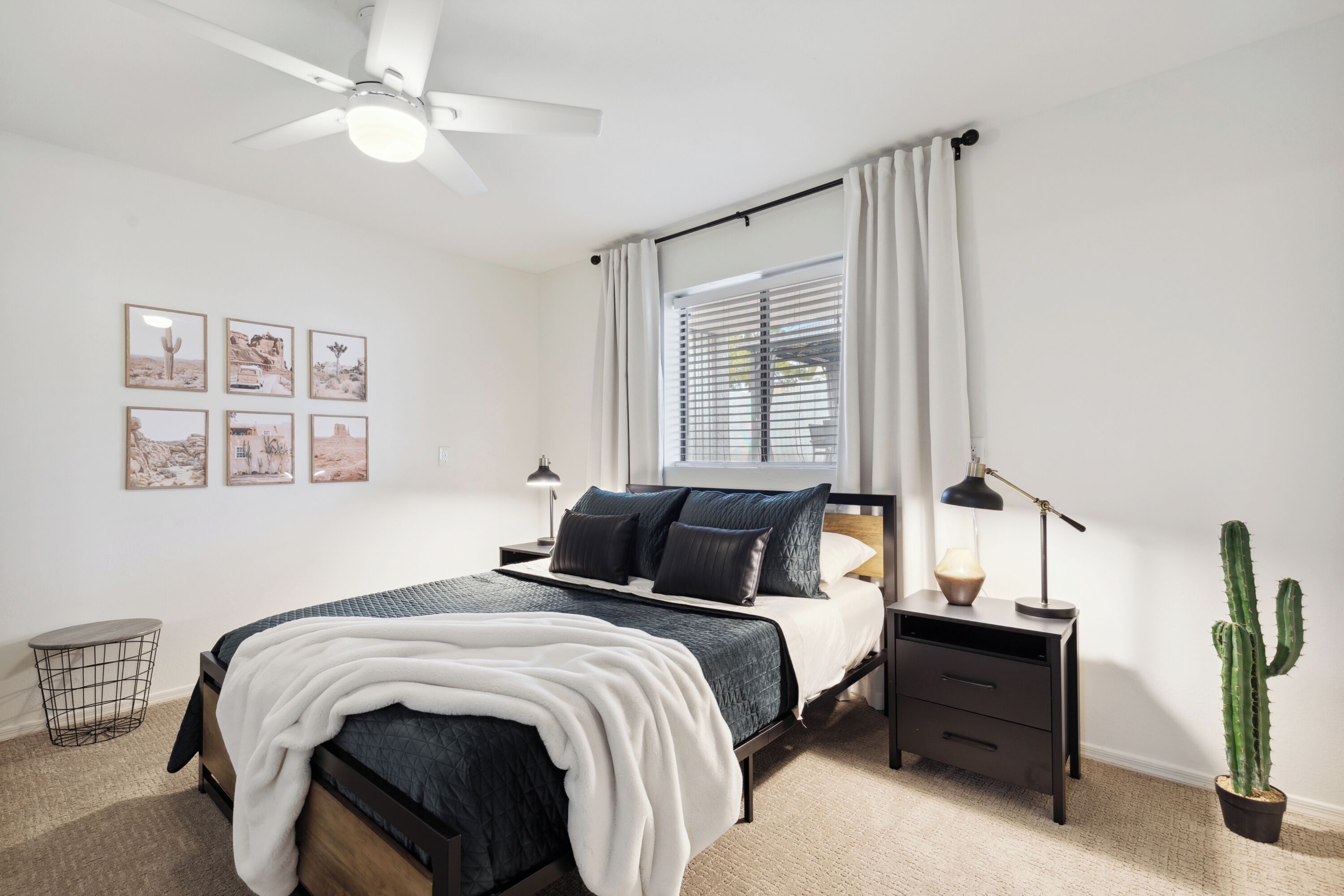 Une chambre à coucher avec un lit, une table de chevet, une lampe, un cactus et un ventilateur de plafond.