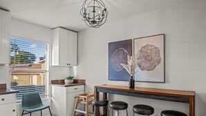 A modern kitchen with white cabinets, a wooden bar counter, and two black stools.