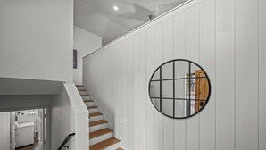 A staircase with wooden steps and white walls, leading to a room with a wooden door and a circular mirror on the wall.