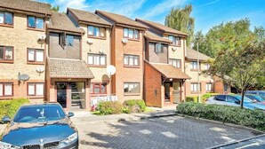 A row of brick apartment buildings with a paved driveway and parked cars. - Charming 1-Bed Flat in London – 3 Mins to Tube + Free Parking (London)