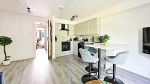 A modern kitchen with white cabinets, a central island with bar stools, and a dining table. - Charming 1-Bed Flat in London – 3 Mins to Tube + Free Parking (London)