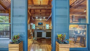 Interior de uma cabana de madeira com área de bar central, soalho em madeira e grandes janelas.