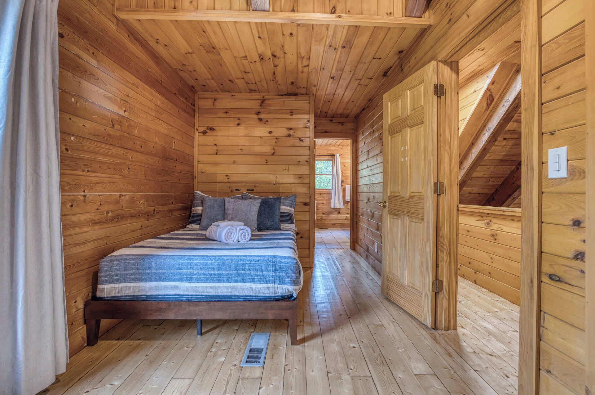 A wooden cabin room with a bed, a door, and a window.