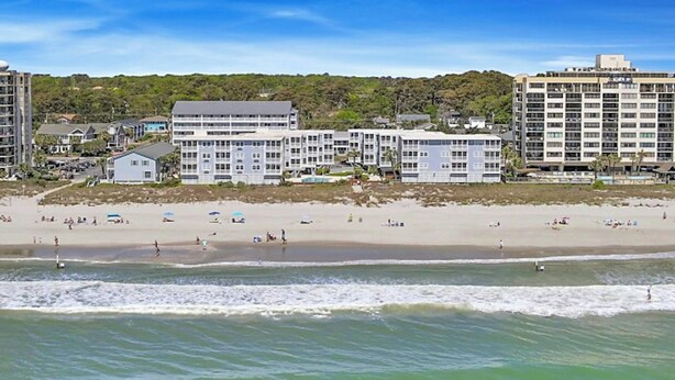 A beachfront hotel with multiple buildings, a sandy beach, and ocean waves. - Palmwood Villas 101- Oceanfront 2BR/2BA- Pool (North Myrtle Beach)