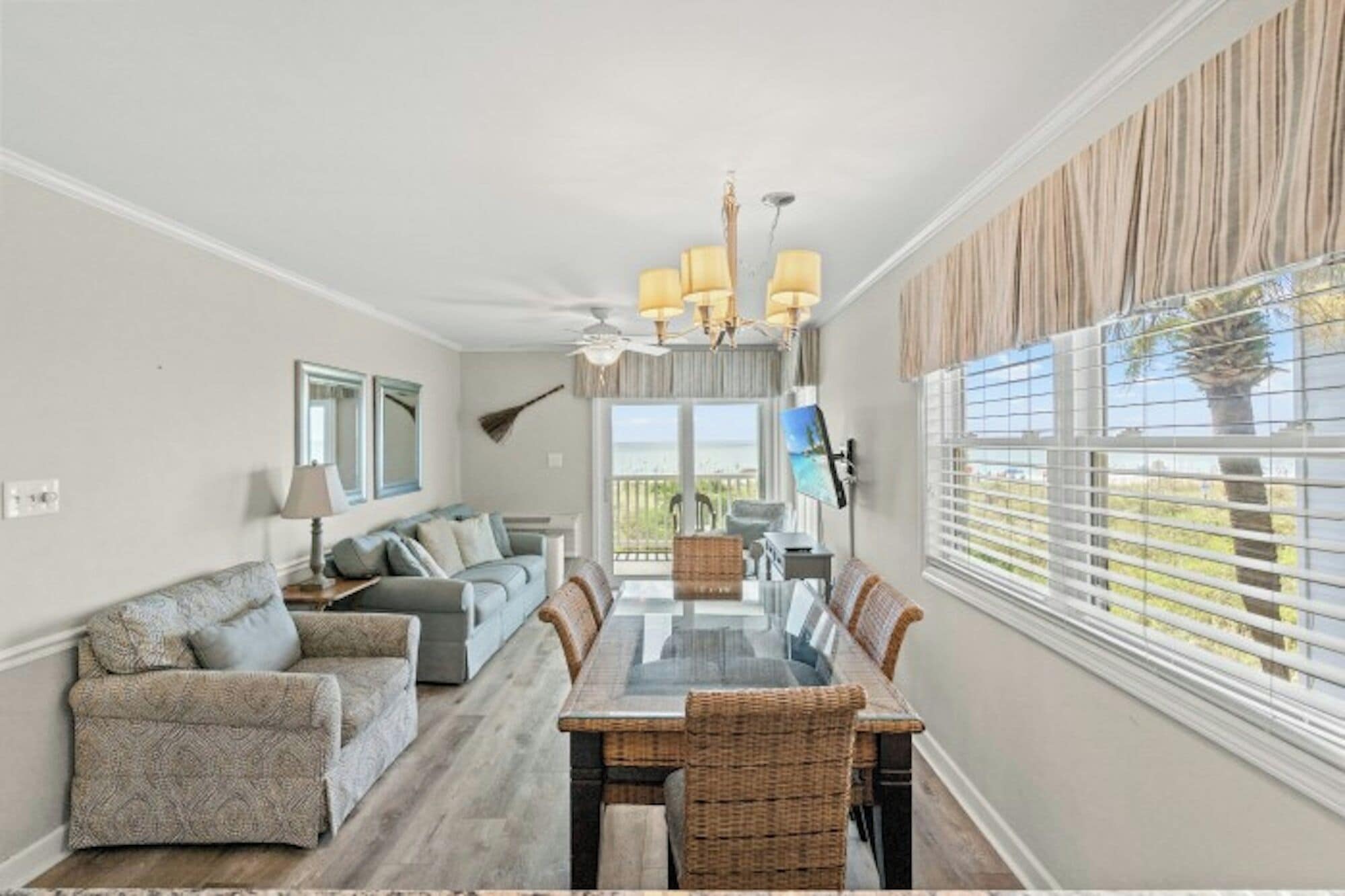 A dining area with a glass table and wicker chairs, a sofa, and a TV on the wall.