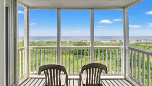 A covered balcony with two wooden chairs facing a beach view. - Palmwood Villas 101- Oceanfront 2BR/2BA- Pool (North Myrtle Beach)