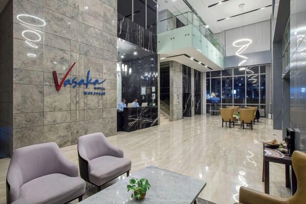 Un moderno hall de hotel con mostrador de recepción, zona de estar y vistas a la ciudad de noche.