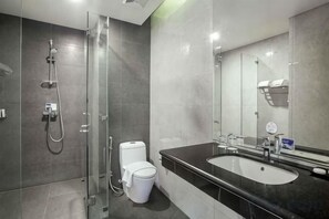 A modern bathroom with a glass shower enclosure, a toilet, and a sink with a large mirror.