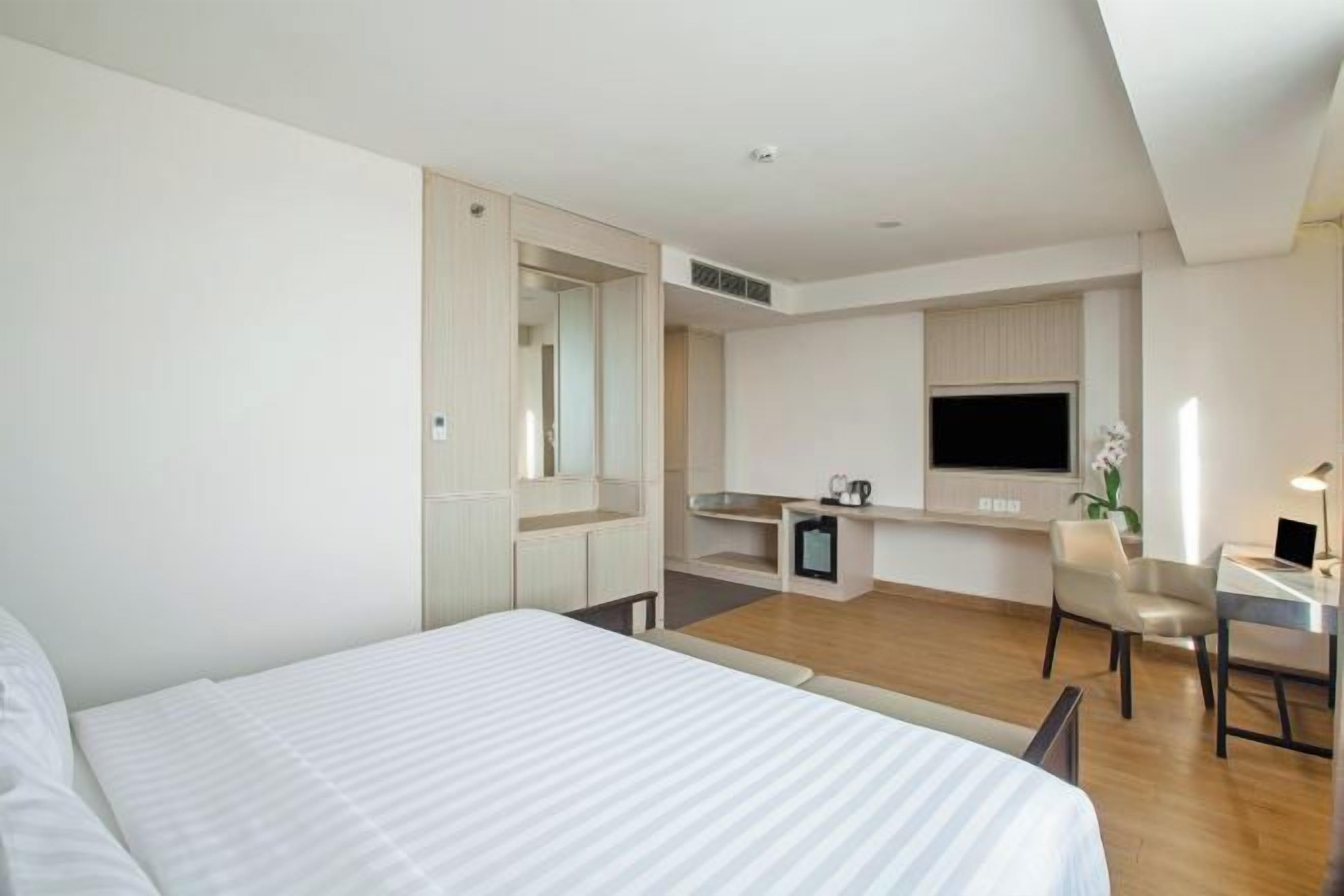 Habitación de hotel con cama, escritorio, silla, televisor y una pequeña kitchenette.