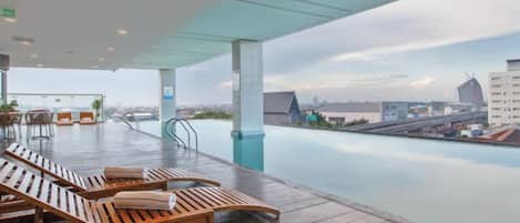 An outdoor infinity pool area with lounge chairs and a city view.
