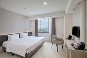 Una habitación de hotel con cama, escritorio con computadora, silla, televisor y ventana con vista a la ciudad.