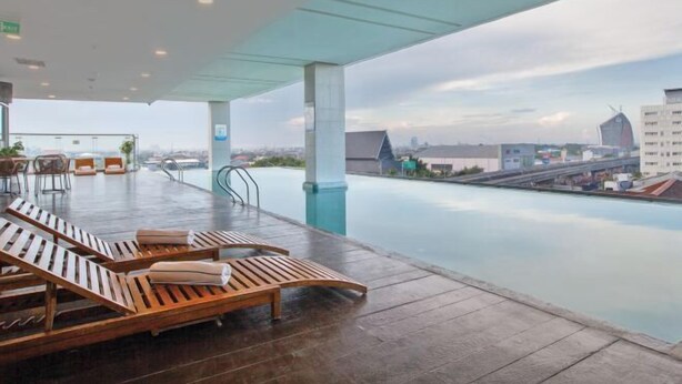 Ein Poolbereich auf dem Dach mit Holzliegen und Blick auf die Stadt.