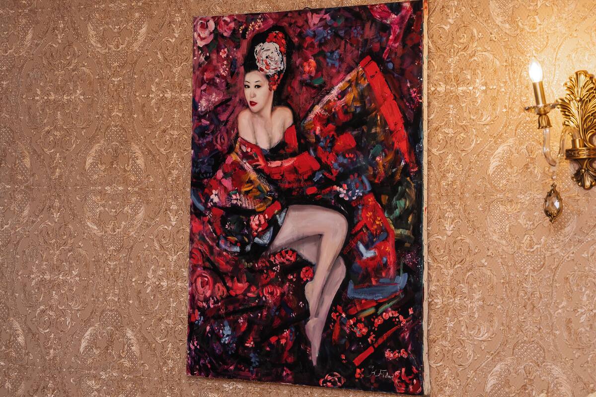 Une pièce dans laquelle on trouve un grand tableau représentant une femme en robe rouge, un lustre et un lit avec une tête de lit blanche.