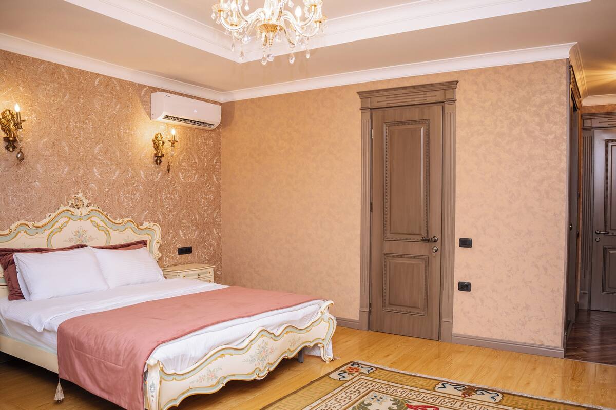 Une chambre à coucher avec un grand lit, un lustre, un appareil de climatisation et une porte en bois.