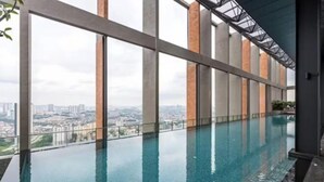 Una piscina infinita interior moderna con vista a la ciudad, ventanas amplias y una barrera de vidrio.