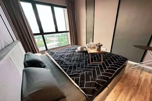 Une petite pièce comprenant un lit, une petite table avec une bouteille et une fenêtre avec des rideaux.